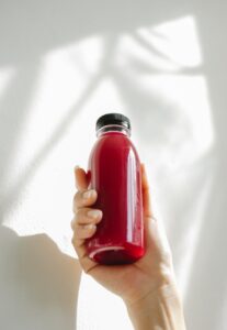 unrecognizable woman holding bottle of red juice against white wall
